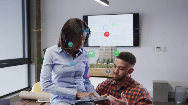 Tapping woman blue shirt and man orange checked shirt reviewing tablet at office, discussing plans