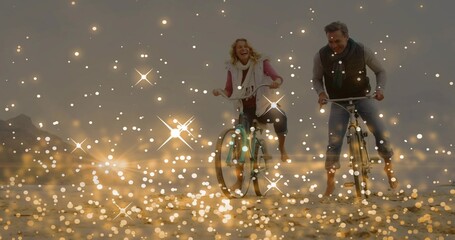 Obraz premium Riding mature couple pedaling bicycles across wet sand at seaside, golden bokeh overlay and scarves
