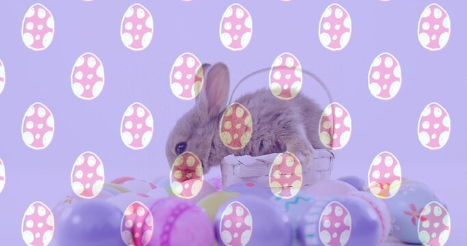 Sitting small brown rabbit on tabletop among whitewashed wicker basket, pastel eggs and egg-overlay
