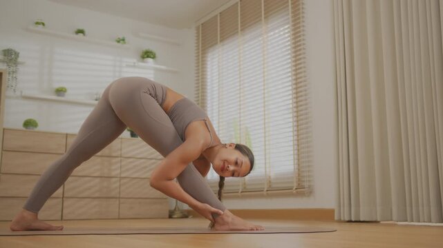 Asian woman yoga stretching pose in bright home interior with calm focus, flexible body, soft window light, home studio fitness wellness exercise scene