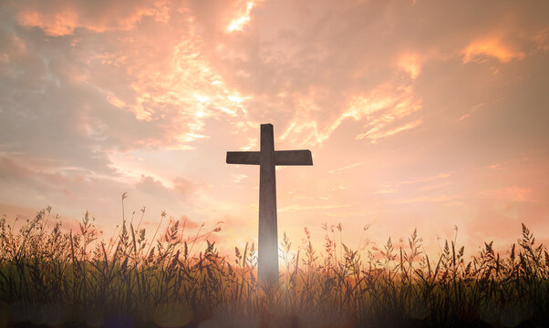 Christian cross silhouette in meadow at sunset with dramatic golden sky.