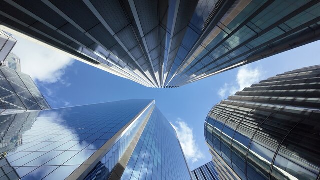 Modern city skyscrapers standing tall, reflecting the blue sky and clouds on their glass facades, creating a sense of urban development and upward progress in a bustling financial district