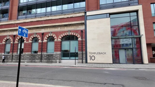 Bristol, UK - May 10 2025: A youth rides a skateboard along the pavement past an old Victorian industrial building repurposed into an office block, as the camera pans toward a more modern block of pas