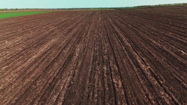 Low Altitude Flyover Plowed Soil Rows, Deep Furrows And Rich Brown Texture Stretching To Horizon, Dynamic