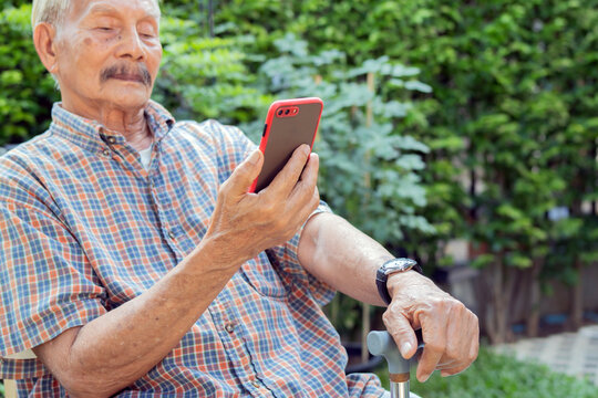 Happy senior man with walking cane using his smart phone in the park.
