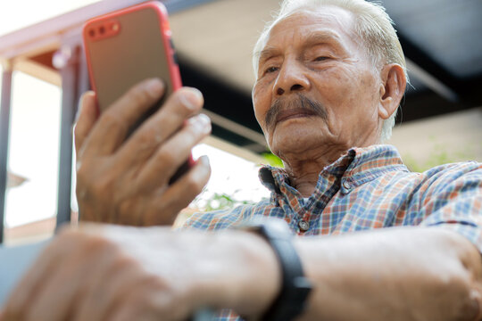Portrait of happy senior man holding walking stick while using a smartphone at home.