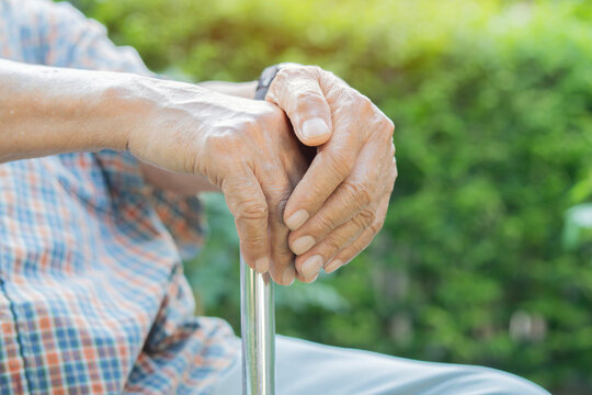 Side view close-up of senior man sitting at park and leaning on walking stick