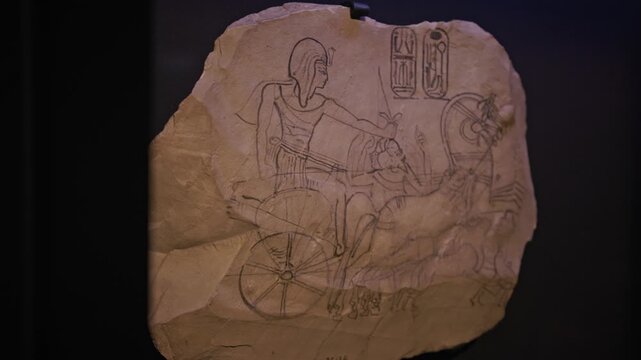 Close-up of an ancient Egyptian drawing depicting a warrior riding a horsedrawn chariot, sketched on a papyrus or limestone fragment with visible hieroglyphs.