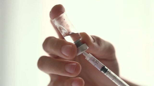 Medical professional aspirating medicine from a glass vial into a syringe against a white background