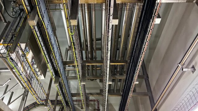 Complex network of stainless steel pipes cable trays and colored wiring covering industrial facility ceiling in food processing or pharmaceutical plant