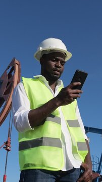 Industrial Site Worker Oversees Shipments With Digital Tools And Safety Gear. Field Technician Utilizes Mobile Applications To Organize And Monitor Port Activities While Ensuring Safety Protocols