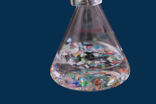Scientific flask containing water and colorful microplastic particles, representing environmental pollution