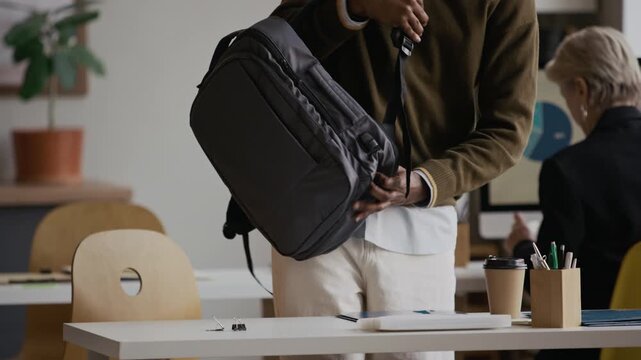 Zoom in of young African American male manager greeting female colleague, taking seat, taking laptop out of backpack and starting workday