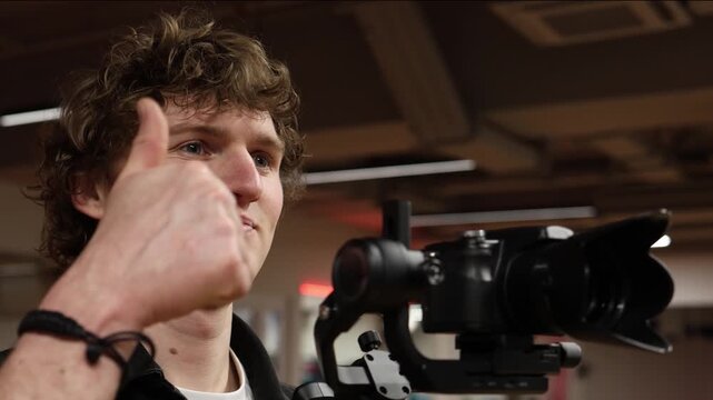 Videographer gives thumbs up near camera on stabilizer confirming successful shot showing confidence satisfaction and positive result after filming session in modern indoor studio environment
