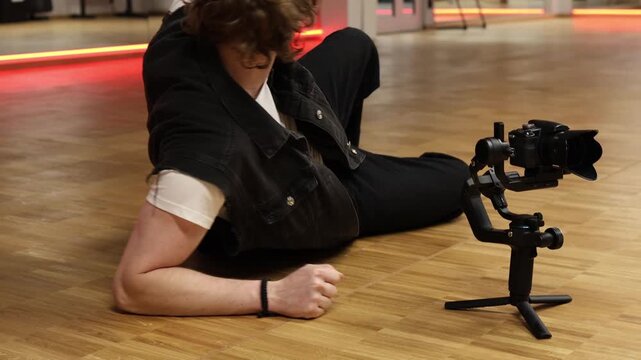 Videographer lies on floor next to camera on stabilizer showing fatigue frustration and stress during filming practice expressing burnout pressure and desire to stop work in indoor studio environment