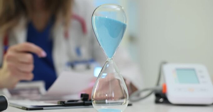 Hourglass stands on medical desk near monitor and clipboard. Doctor writes notes tracking time and plans next patient check with steady focus