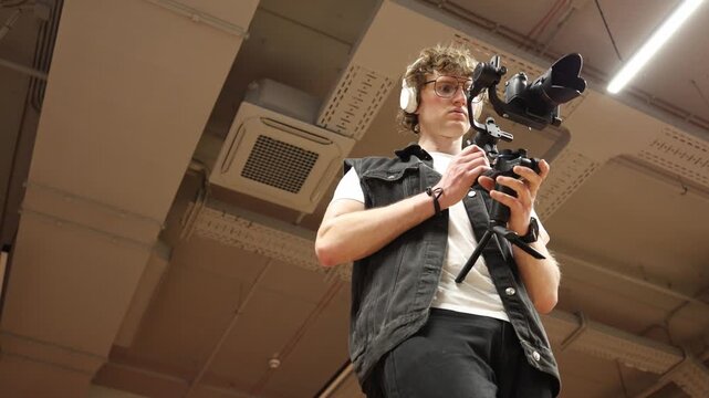 Videographer adjusts camera on gimbal focusing on balance control and stabilization preparing gear for smooth motion and precise cinematic filming in professional indoor studio environment