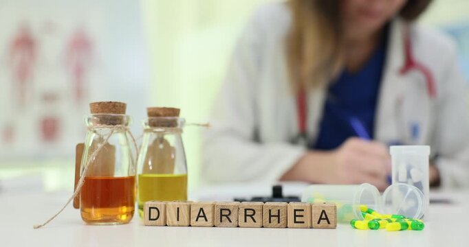 Wooden blocks spell Diarrhea near medicine bottles and capsules on desk. Doctor writes record reviewing dehydration risks while selecting care plan