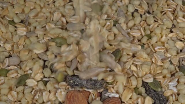Macro shot of dry granola mix pouring slowly close-up view of falling healthy breakfast cereal and seeds