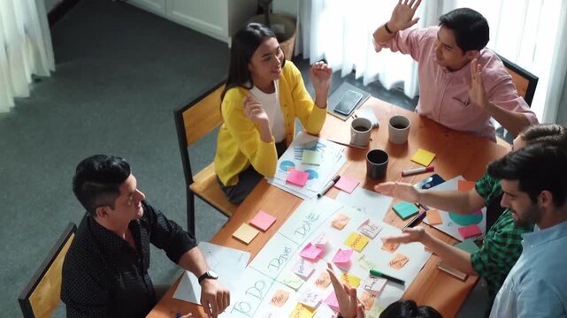 Top view of creative start up team giving high five to encourage their teamwork or successful project while making scrum task board for managing workflow by using marker and sticky notes. Convocation.