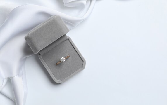 Top view of angagement ring in a velvet box with satin fabric on white background