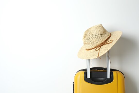 Suitcase with stylish wicker hat near white wall. Travel concept. Space for text