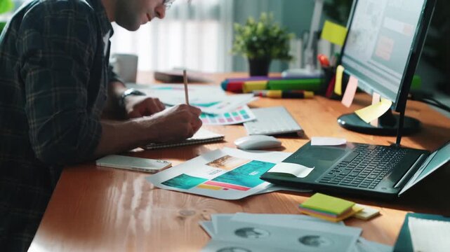 Interior designer looking at laptop and designing color while looking at palette at meeting table with laptop, computer and paper placed. Close up of business man working on color design. Symposium.