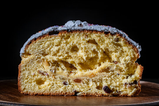 Sliced traditional Easter paska cake or panettone with white icing and raisins on a wooden board against a dark background. Great for festive food and holiday concepts