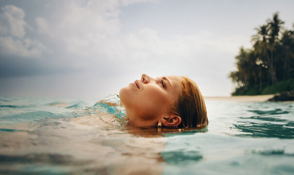 Young woman floating in clear tropical water near a sunny beach palm trees