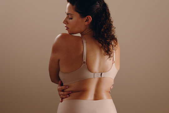 Woman embracing herself in beige bra, back view