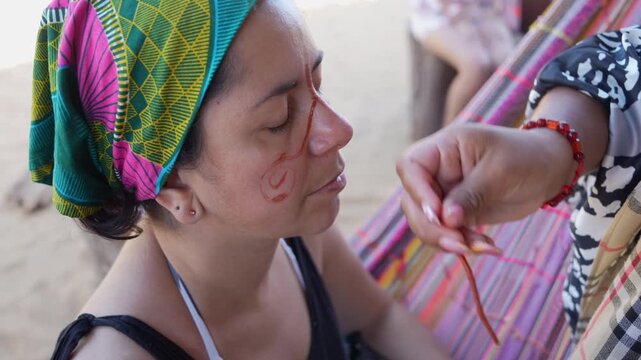 Close-up shot of Wayuu women in La Guajira, Colombia, applying traditional face paint using natural pigments. Vibrant textiles, ethnic patterns, and natural daylight enhance cultural detail.