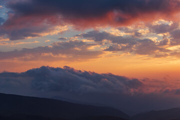 Obraz premium Calm evening sky with soft golden light and layered clouds above dark mountain silhouettes in Georgia, creating a peaceful and atmospheric landscape. 