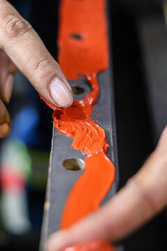 Close up of a mechanic's finger spreading red high-temperature RTV silicone sealant on a metal engine component for a precise leak-proof seal. Professional industrial maintenance and repair.