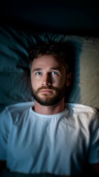 A man lying awake in bed at night, looking thoughtful and unable to sleep.