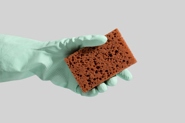 Female hand in rubber glove with brown cleaning sponge on grey background
