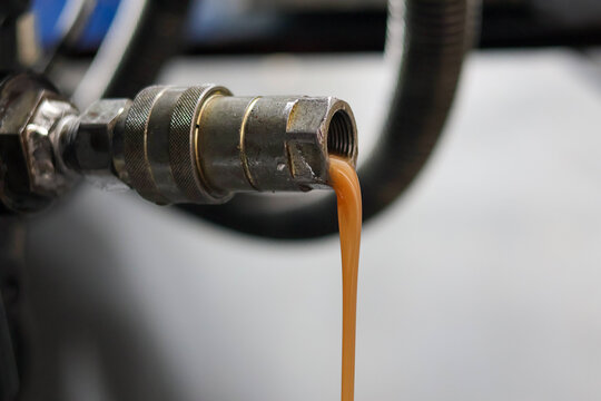 Close up of milky brown contaminated hydraulic oil draining from a metal quick release coupler. Indicates water contamination or emulsion in a heavy machinery fluid system.
