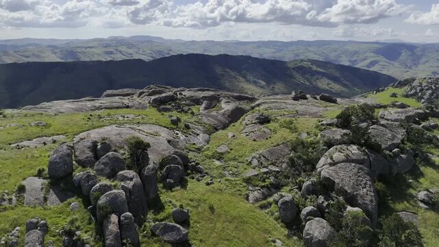 Drone orbits right over rocks on edge cliff overlooking valley on a sunny day at Sibebe Rock near Mbabane, Eswatini