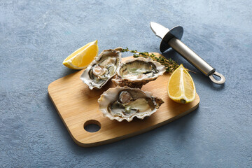 Wooden board with delicious fresh oysters, thyme and lemon on blue background, closeup © Pixel-Shot
