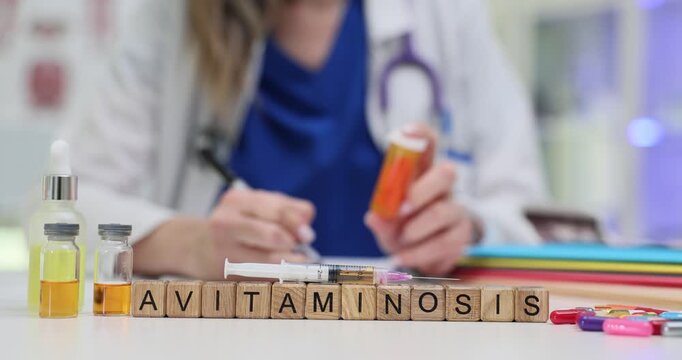 Text Avitaminosis on wood blocks with flasks syringe and pills in hospital. Female physician prescribes to take multivitamins to patient in clinic