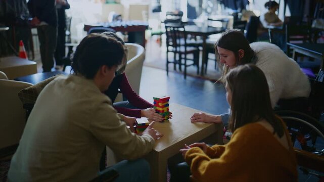 A group of students is focused on playing a stacking block game at a table. Young people enjoy a collaborative and challenging activity in a casual setting.