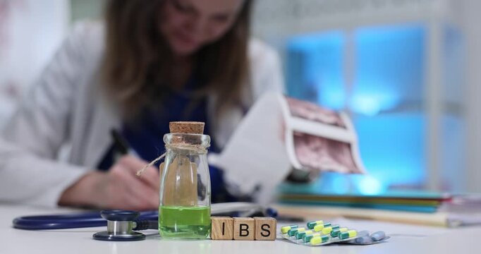 IBS abbreviation on wooden blocks among medications and stethoscope in clinic. Female doctor analyzes patient ultrasound scans in hospital