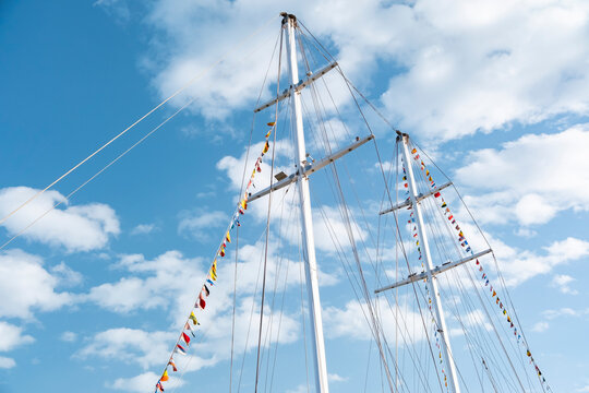 Tall ship sails against blue sky with clouds and colorful flags flying high in the air in a marina setting
