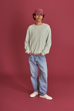 Stylish young man showcases modern fashion against a vivid maroon backdrop