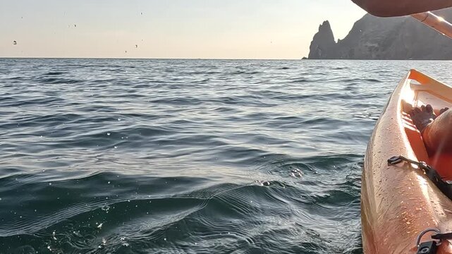 Kayaking, ocean, paddle person propels orange kayak through calm sea water, enjoying serene coastal view with majestic rock formations