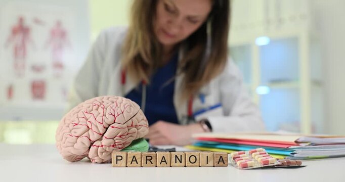 Text Paranoia on wood cubes with pills and brain anatomical model in hospital. Female psychiatrist diagnoses mental health disorder in medical office