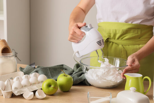 Woman whipping egg albumen with mixer at table in kitchen