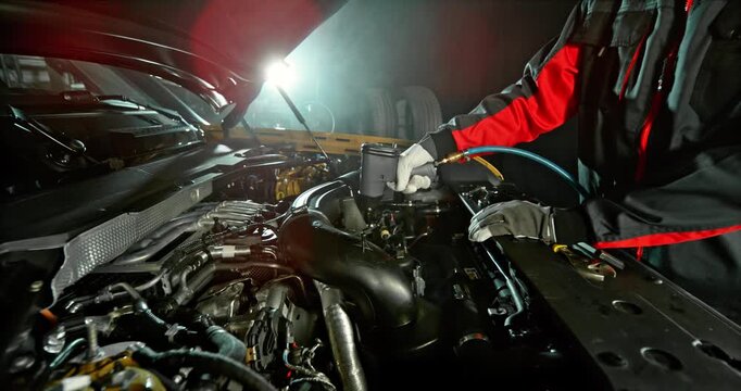 Slow motion shot of mechanic working on car engine with camera movement above engine, dramatic lighting in workshop. Automotive repair concept, maintenance and service.
