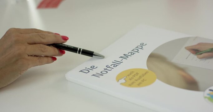 Close-up of a hand with red nail polish holding a pen over a German emergency folder (Die Notfall-Mappe)