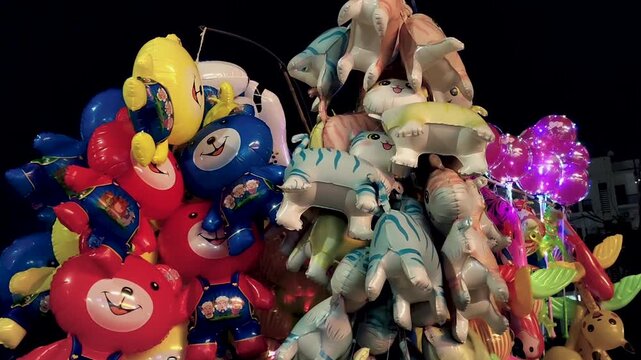 Bright helium balloons shaped like bears and animals glowing at night fair. Ideal for festival, carnival, childhood joy, street market, celebration and festive atmosphere visuals.