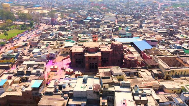 High-angle aerial shot of the historic Govind Dev Ji Temple in Vrindavan, with colorful pink powder visible on the ground during the Holi festival celebrations.